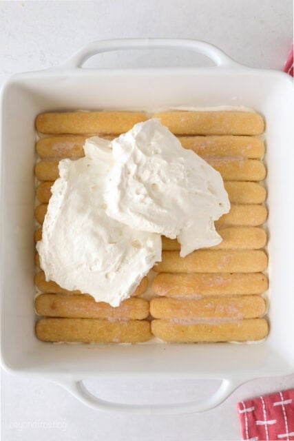 Ladyfingers laying in a pan with a pile of whipped cream on top