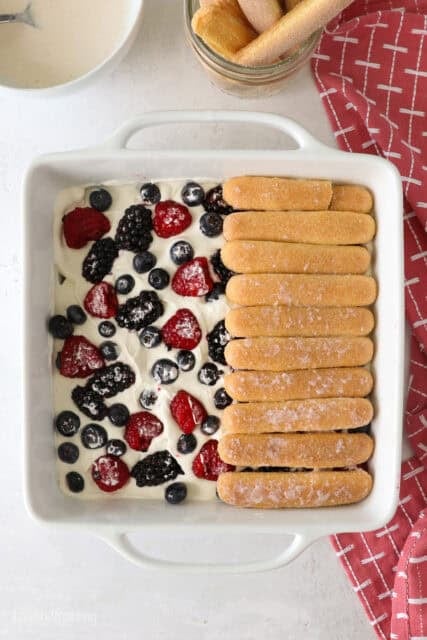 Overhead shot showing the process of layering ladyfingers overtop of berry and whipped cream