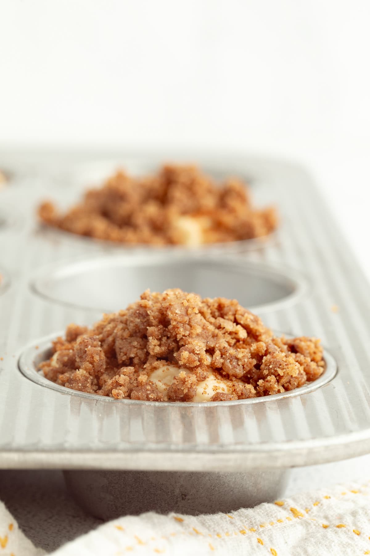 Close up of muffin batter topped with streusel inside the well of a muffin pan.