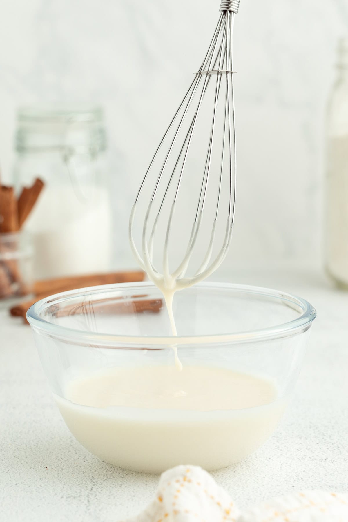 A whisk held over a bowl of cream cheese glaze.