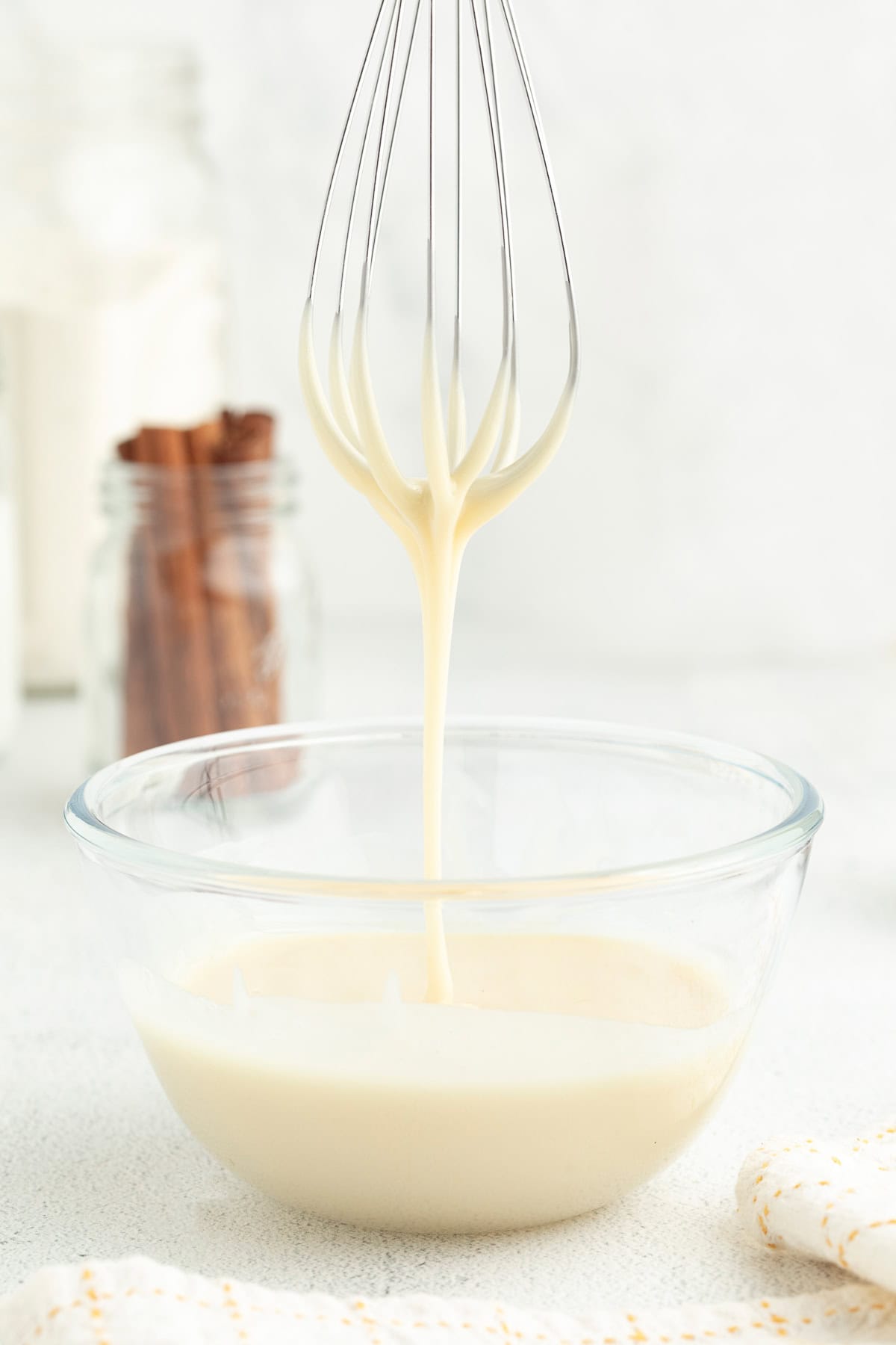 Maple glaze drizzling from the end of a whisk held over a bowl of glaze.
