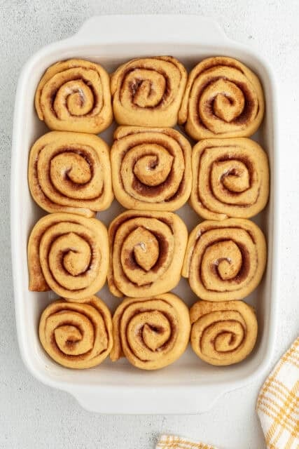 Overhead view of unbaked pumpkin cinnamon rolls in a ceramic baking dish.