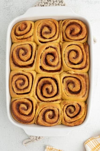 Overhead view of freshly baked pumpkin cinnamon rolls in a ceramic baking dish.