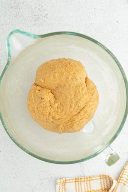 A large ball of pumpkin cinnamon roll dough in a glass bowl.