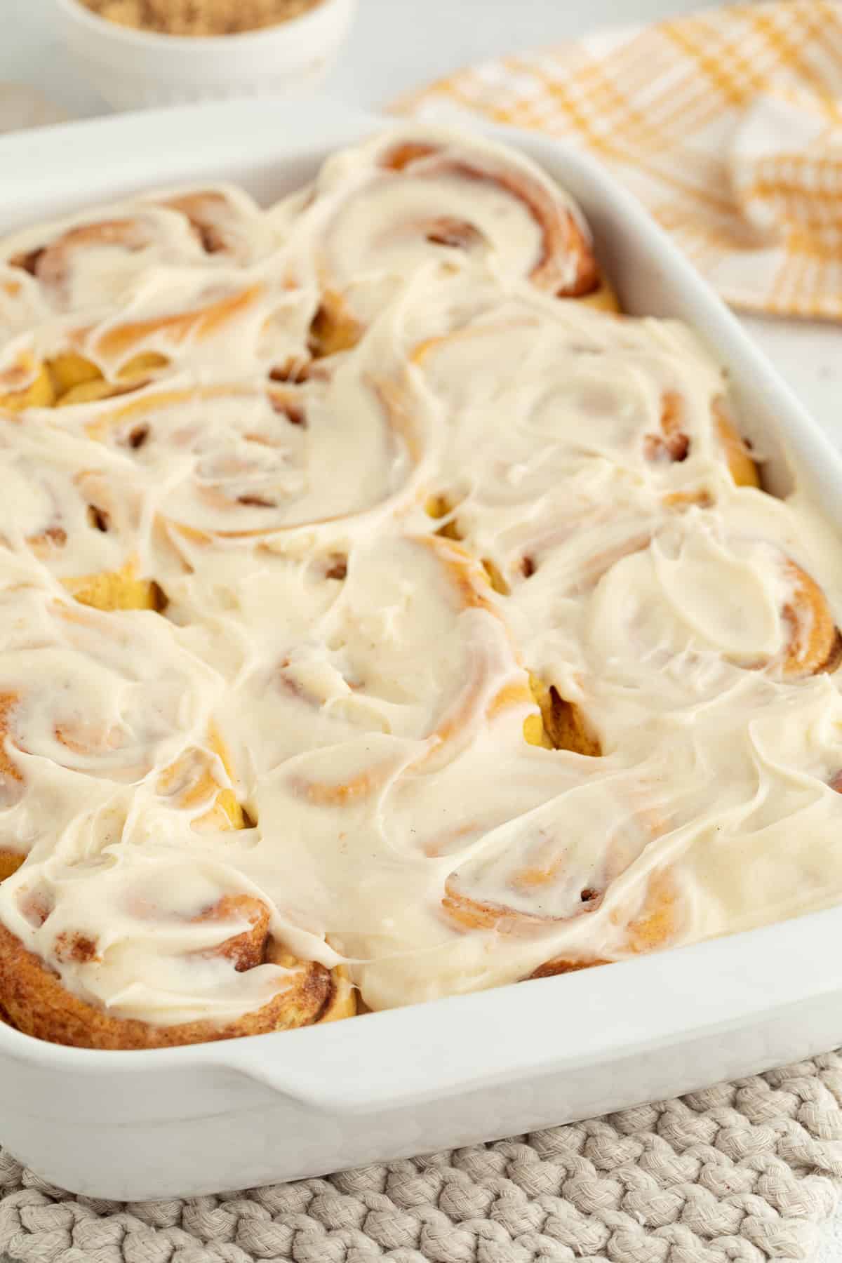 Pumpkin cinnamon rolls with cream cheese frosting in a white ceramic baking dish.