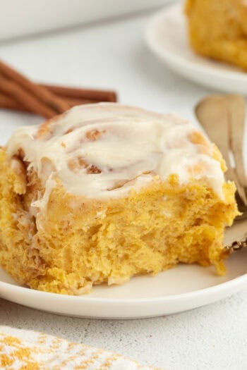 A pumpkin cinnamon roll with cream cheese icing on a plate next to a fork.