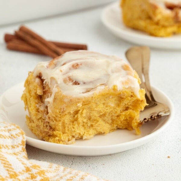 A pumpkin cinnamon roll with cream cheese icing on a plate next to a fork.