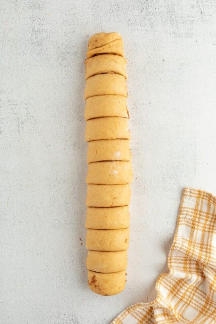 Pumpkin cinnamon roll dough rolled up into a log and sliced into rolls.
