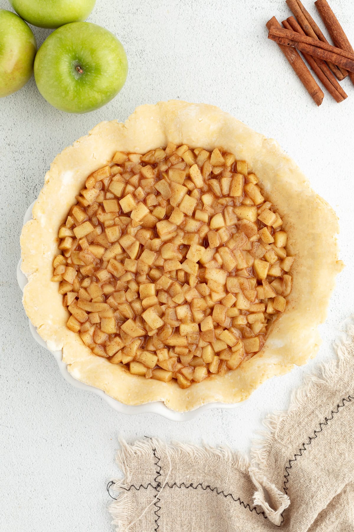 Overhead view of a pie crust inside a pie plate filled with apple pie filling.