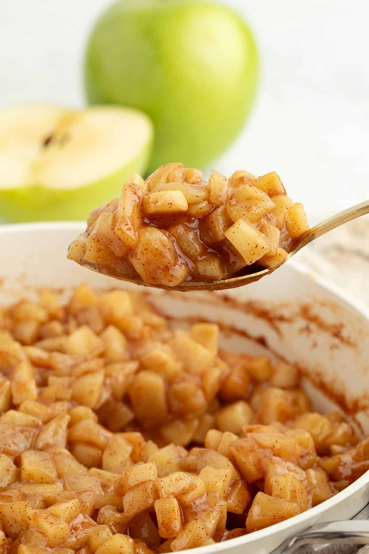A spoonful of apple pie filling held over more filling in a skillet.