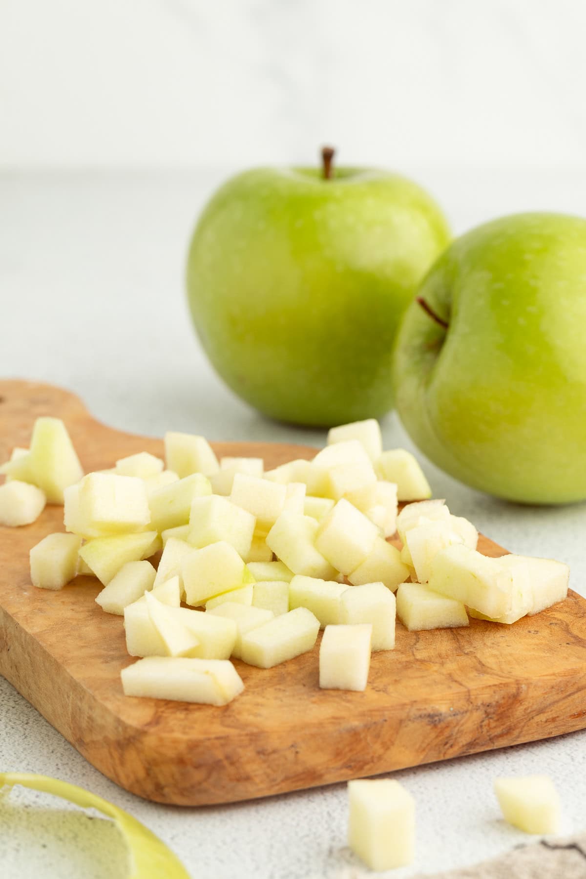 Diced apples on a wooden cutting board with two Granny Smith apples in the background.