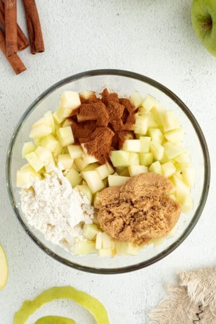 Apple pie filling ingredients combined in a glass bowl.