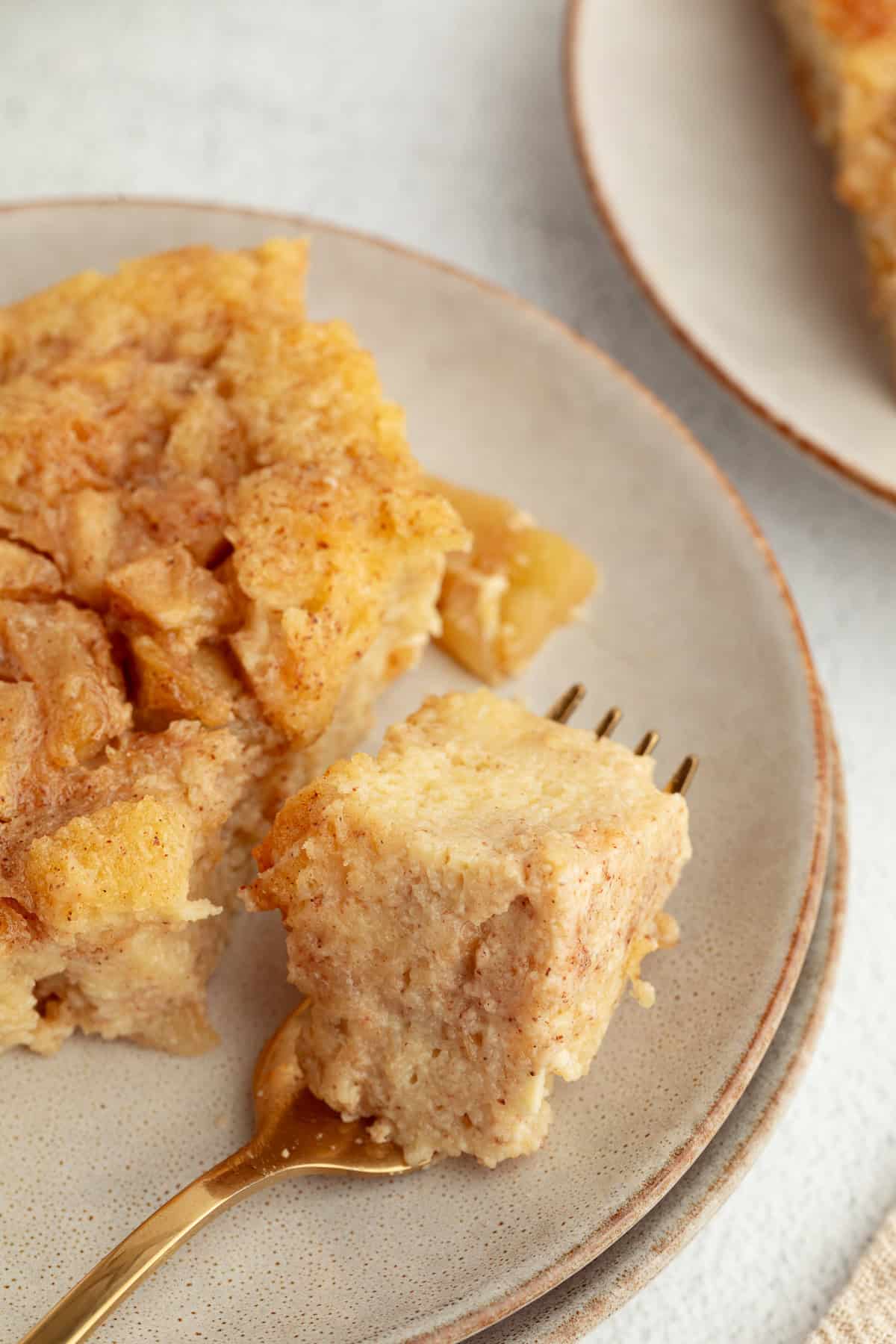 Close up of a forkful of apple bread pudding next to a spice on a plate.