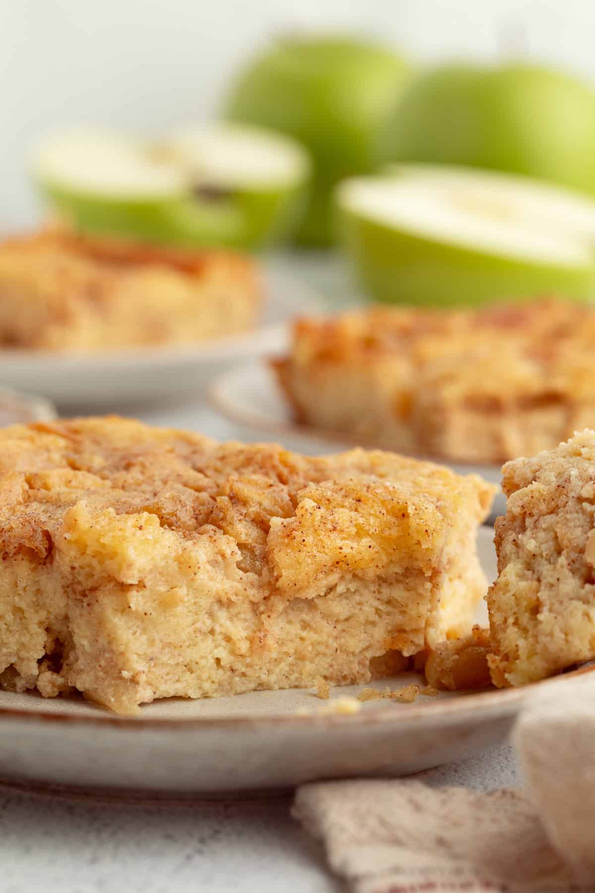 A slice of homemade apple bread pudding on a plate with more slices in the background.
