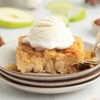 A slice of homemade apple bread pudding topped with ice cream on a plate next to a fork.