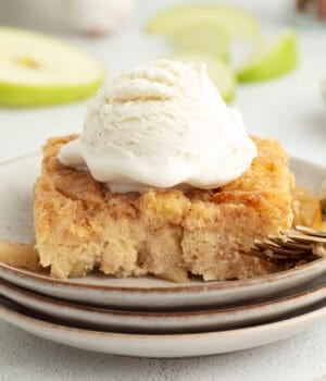 A slice of homemade apple bread pudding topped with ice cream on a plate next to a fork.