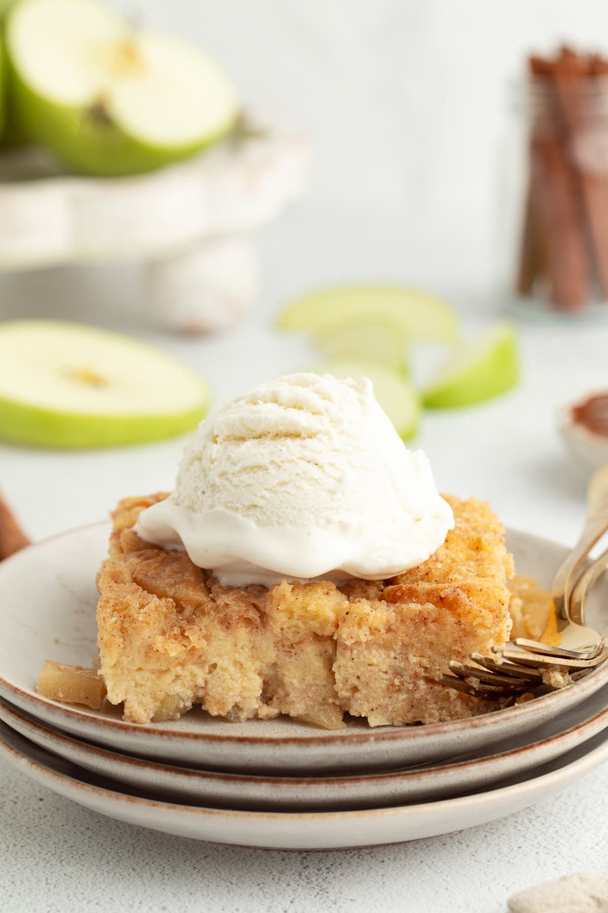 A slice of homemade apple pie bread pudding topped with ice cream on a plate next to a fork.