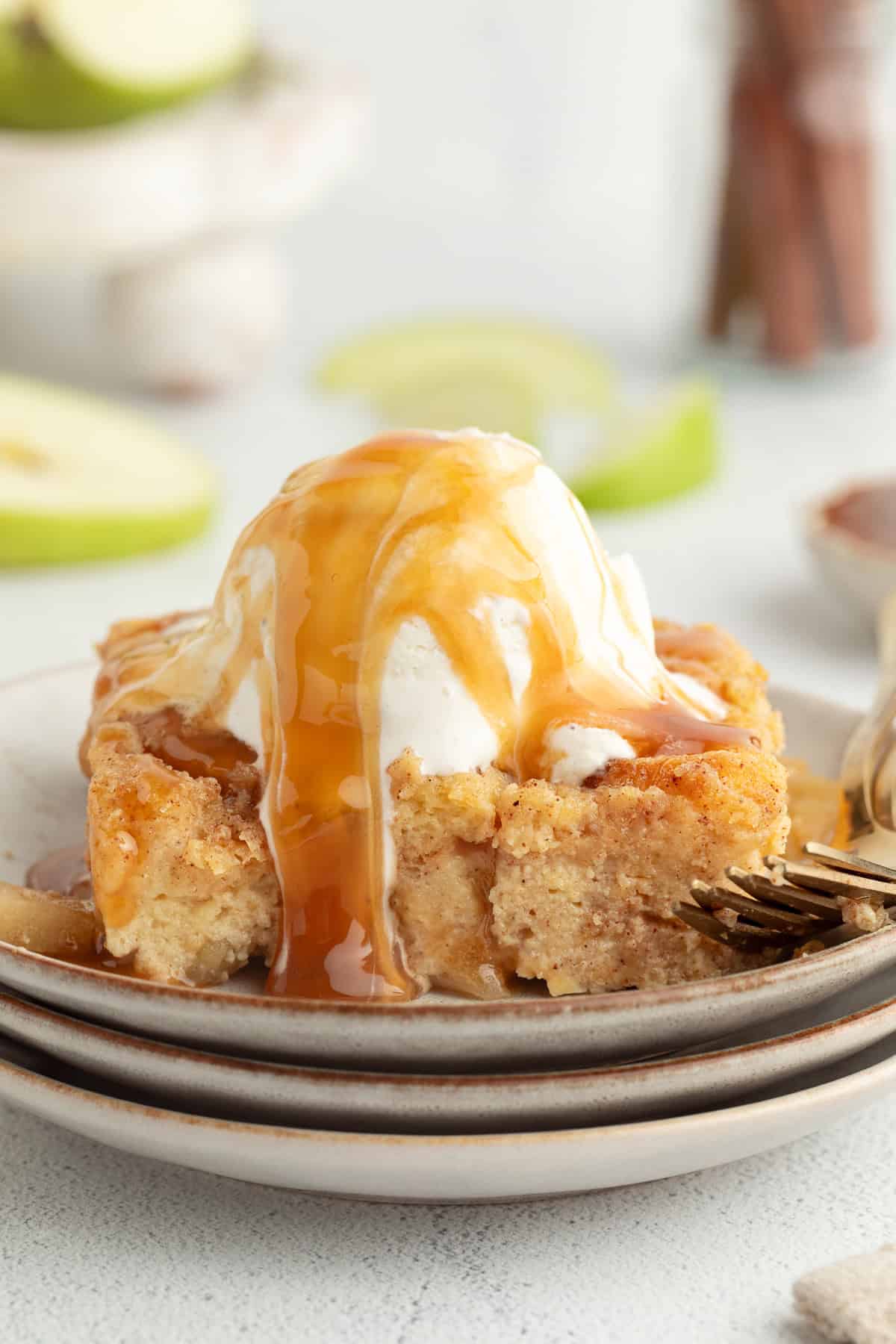 Cozy and full of flavor, this warm apple bread pudding is easy to make with fluffy brioche and tender cinnamon apples baked in creamy custard. A slice of old-fashioned apple bread pudding topped with ice cream and caramel sauce on a plate.
