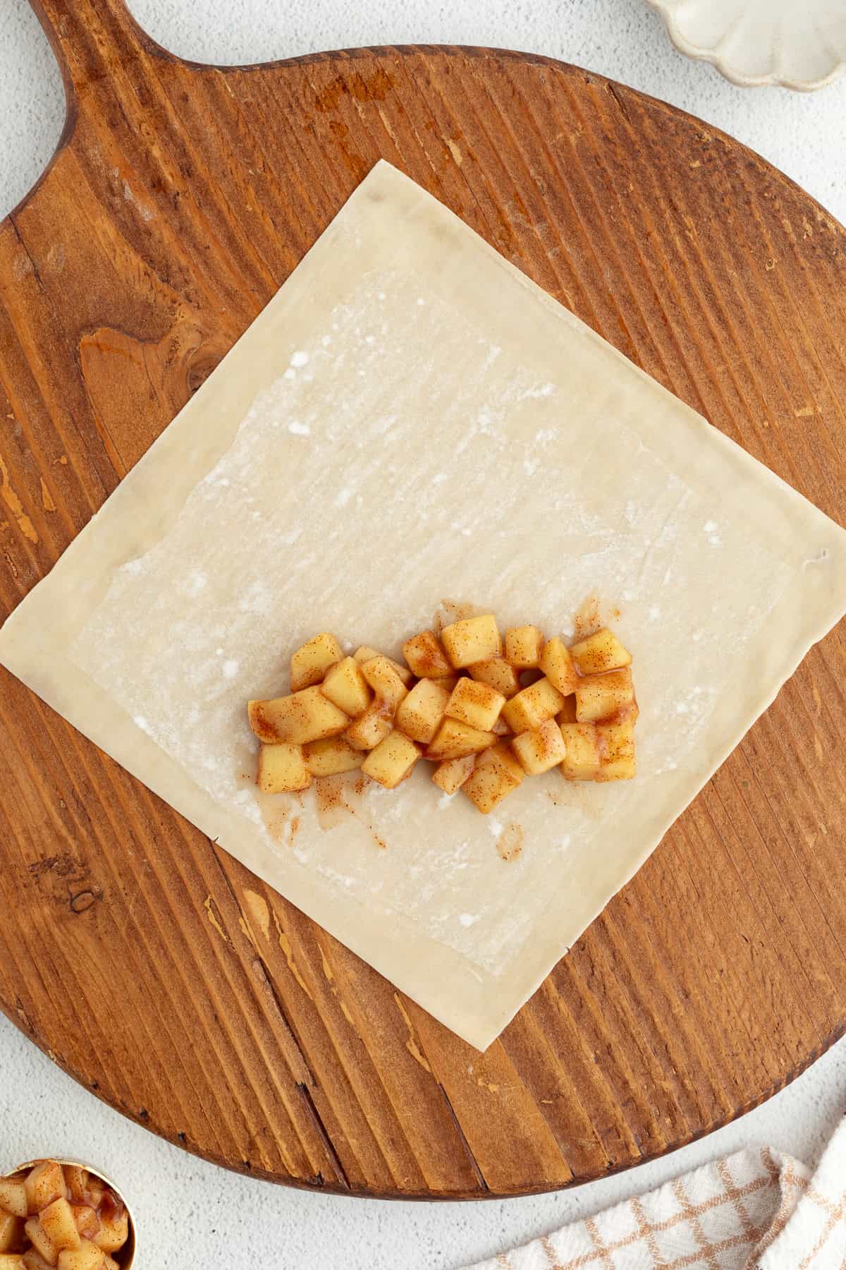 These apple pie egg rolls are golden, crispy egg roll wrappers bursting with homemade apple pie filling. Make them in the oven or air fryer! Apple pie filling added to a wonton wrapper on a wooden cutting board.