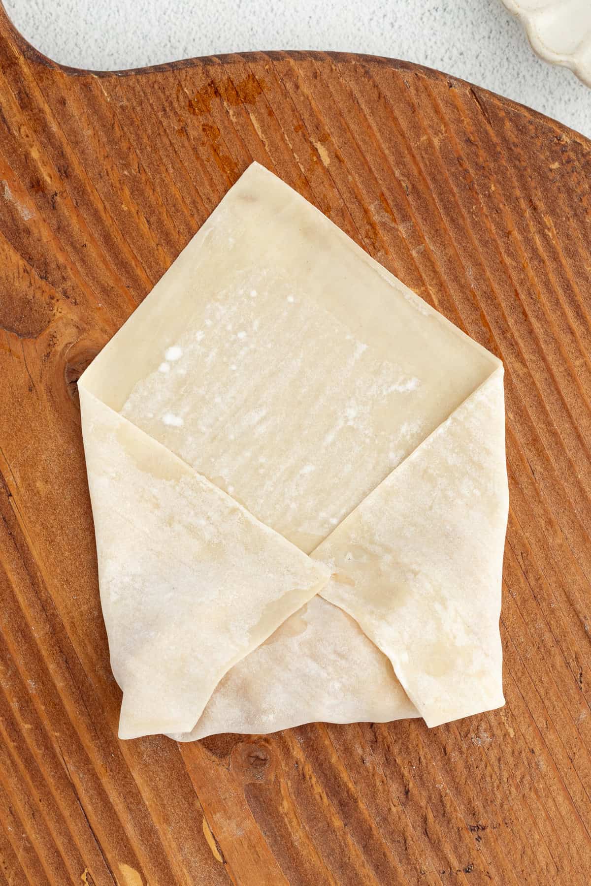 These apple pie egg rolls are golden, crispy egg roll wrappers bursting with homemade apple pie filling. Make them in the oven or air fryer! A partially wrapped apple pie egg roll, showing how to fold in the bottom and sides of the wonton wrapper over the apple pie filling.