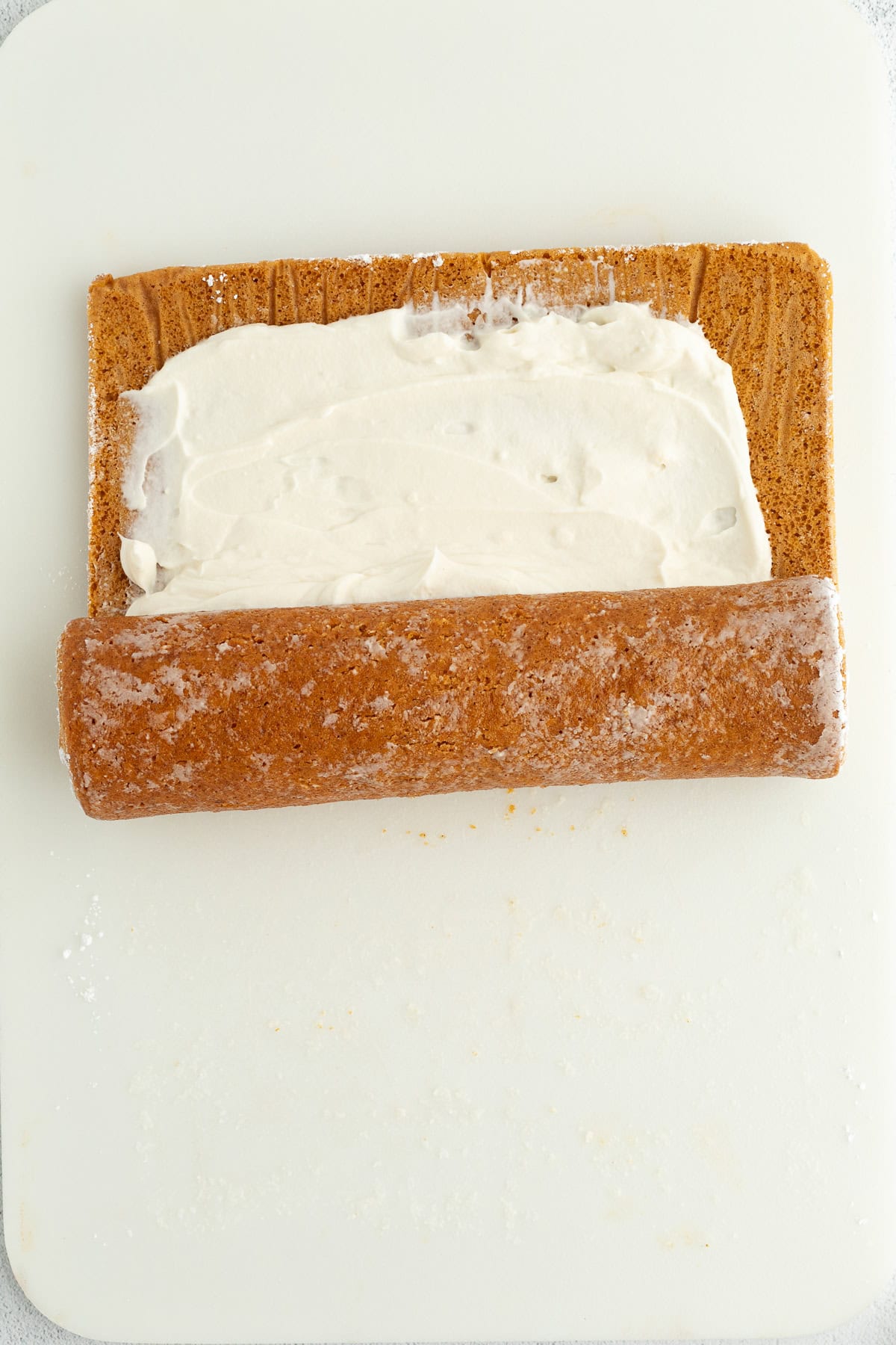 A partially rolled-up pumpkin cake roll on a white surface.