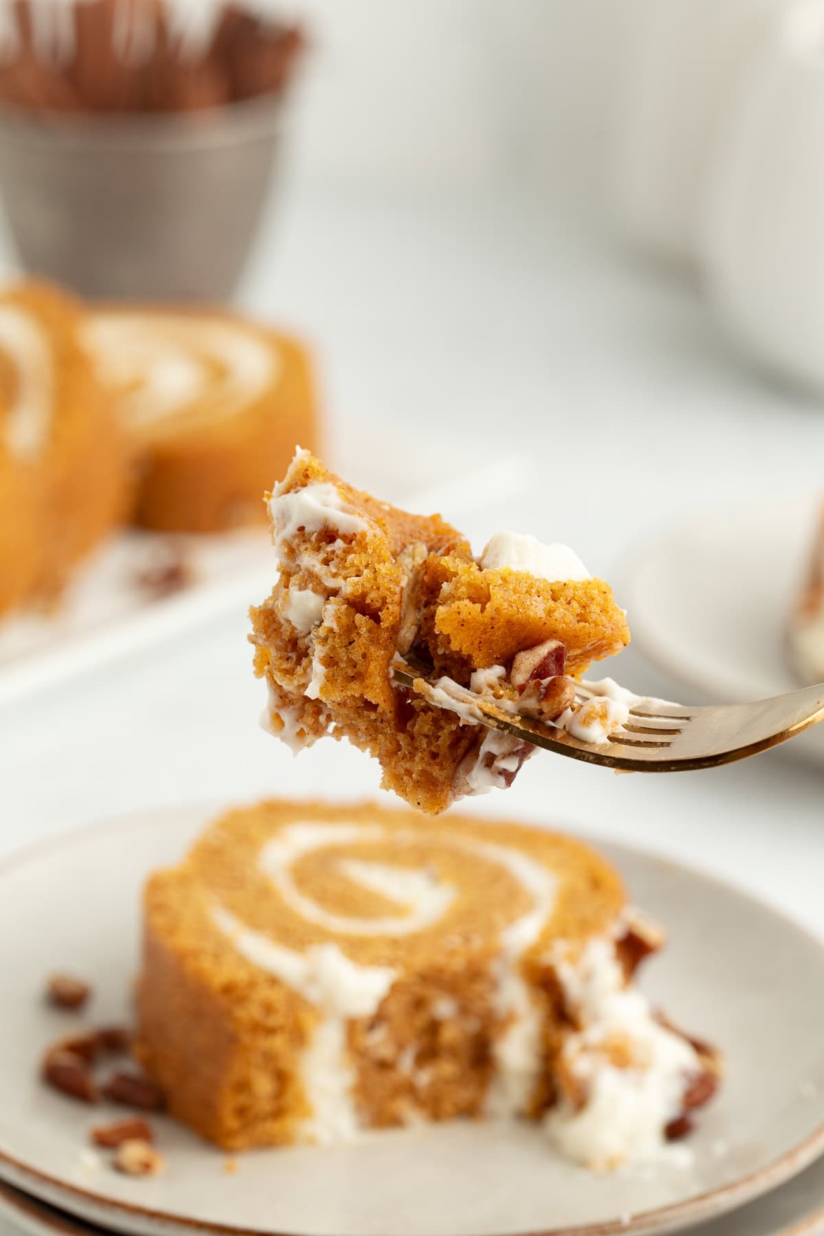 Close up of a forkful of pumpkin cake roll held up in front of a slice of cake on a plate.