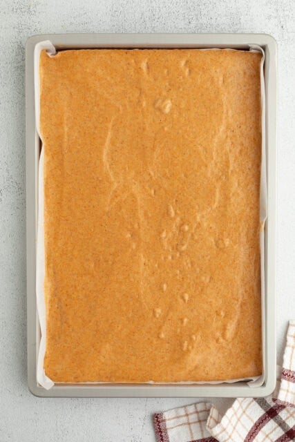 Pumpkin cake batter spread evenly into a lined jelly roll pan.