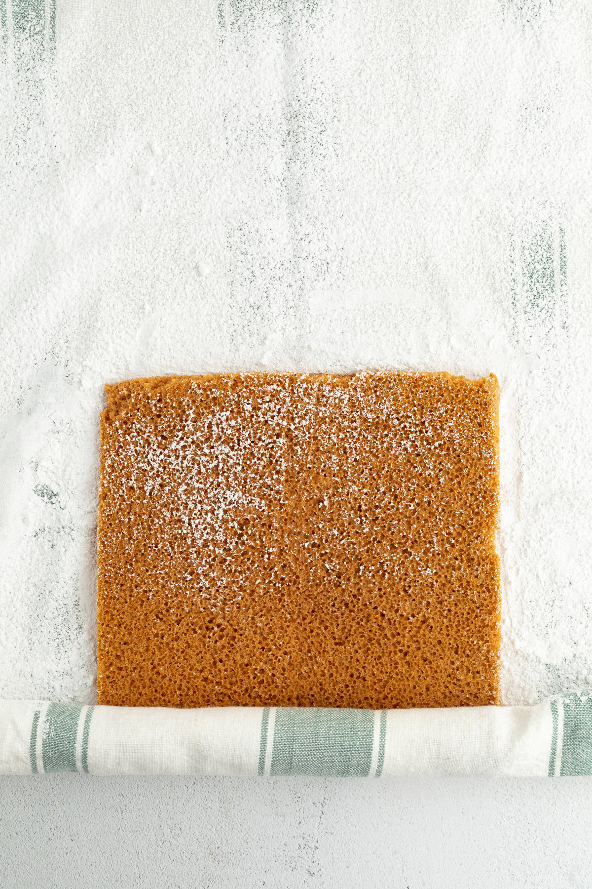 Pumpkin cake partially rolled up inside a tea towel.
