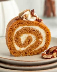 Homemade pumpkin roll topped with whipped cream and chopped pecans on a plate.