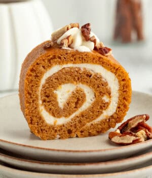 Homemade pumpkin roll topped with whipped cream and chopped pecans on a plate.