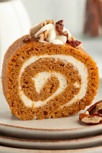 Homemade pumpkin roll topped with whipped cream and chopped pecans on a plate.