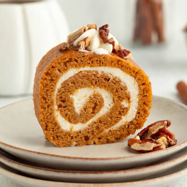 Homemade pumpkin roll topped with whipped cream and chopped pecans on a plate.