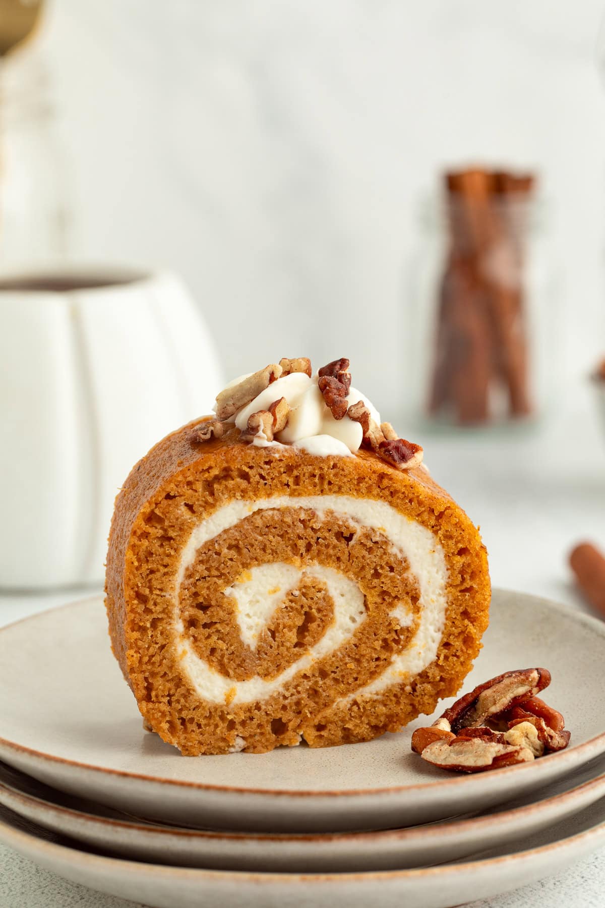 This easy pumpkin cake roll recipe is a soft, spiced cake with creamy mascarpone filling. Learn how to bake and shape a perfect pumpkin roll! Homemade pumpkin cake roll topped with whipped cream and chopped pecans on a plate.