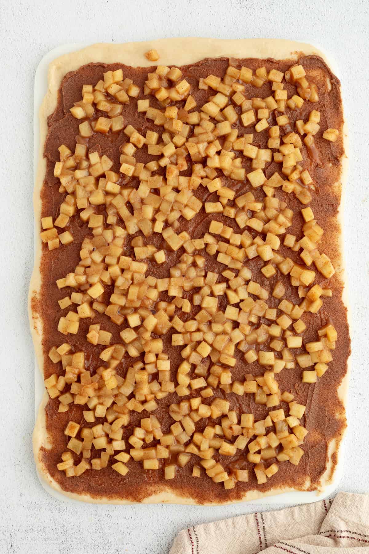 Homemade apple cinnamon rolls are golden-baked with warm cinnamon apple filling and topped with creamy brown butter cream cheese frosting. Cinnamon apple filling spread over rolled out cinnamon roll dough.