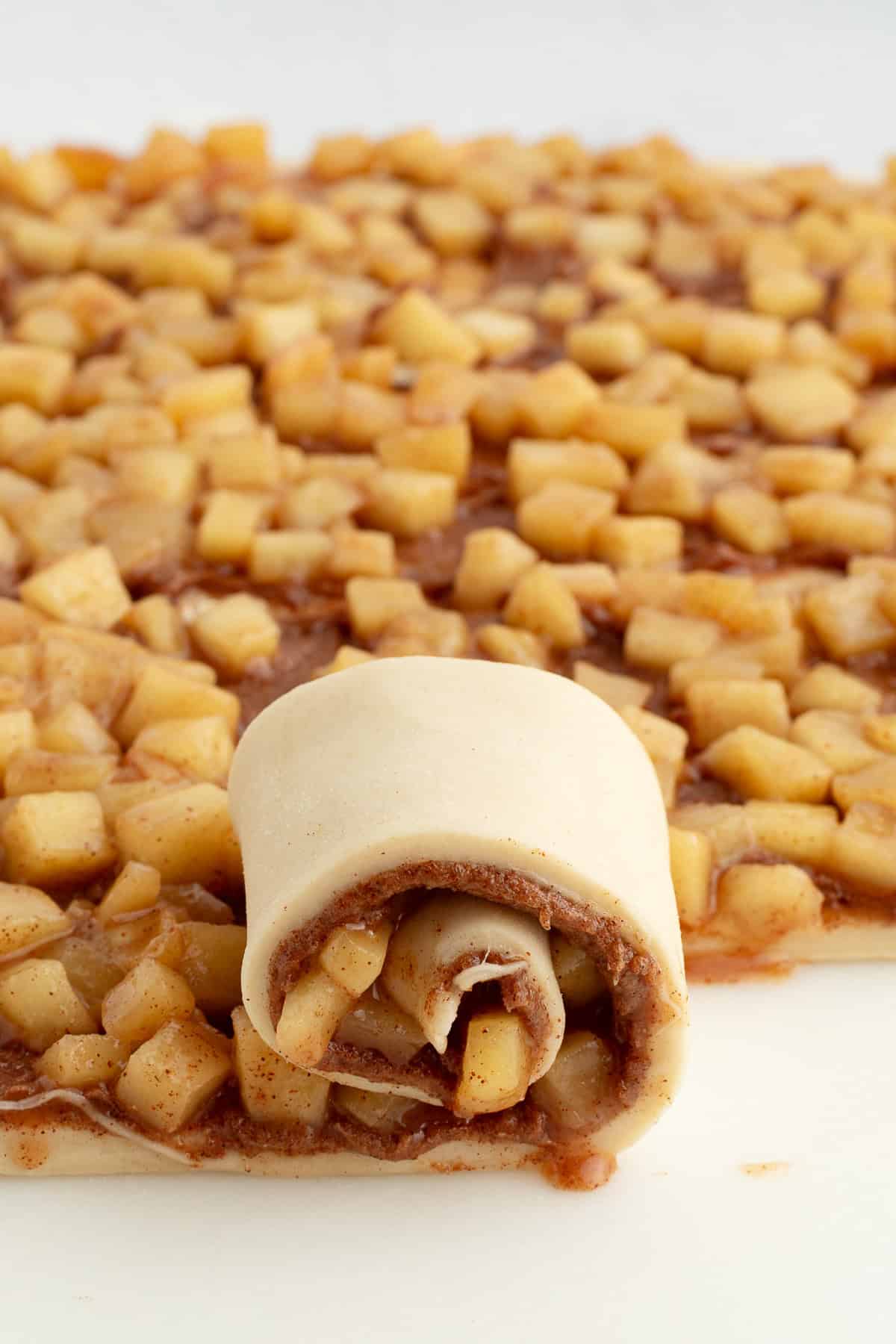 Homemade apple cinnamon rolls are golden-baked with warm cinnamon apple filling and topped with creamy brown butter cream cheese frosting. Cinnamon roll dough being rolled up around apple filling.