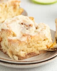 An apple cinnamon roll topped with brown butter cream cheese frosting on a plate.