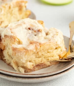 An apple cinnamon roll topped with brown butter cream cheese frosting on a plate.