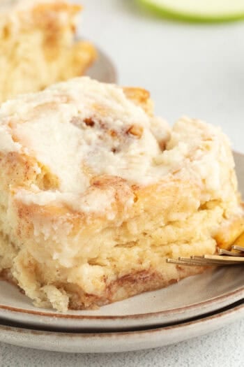 An apple cinnamon roll topped with brown butter cream cheese frosting on a plate.