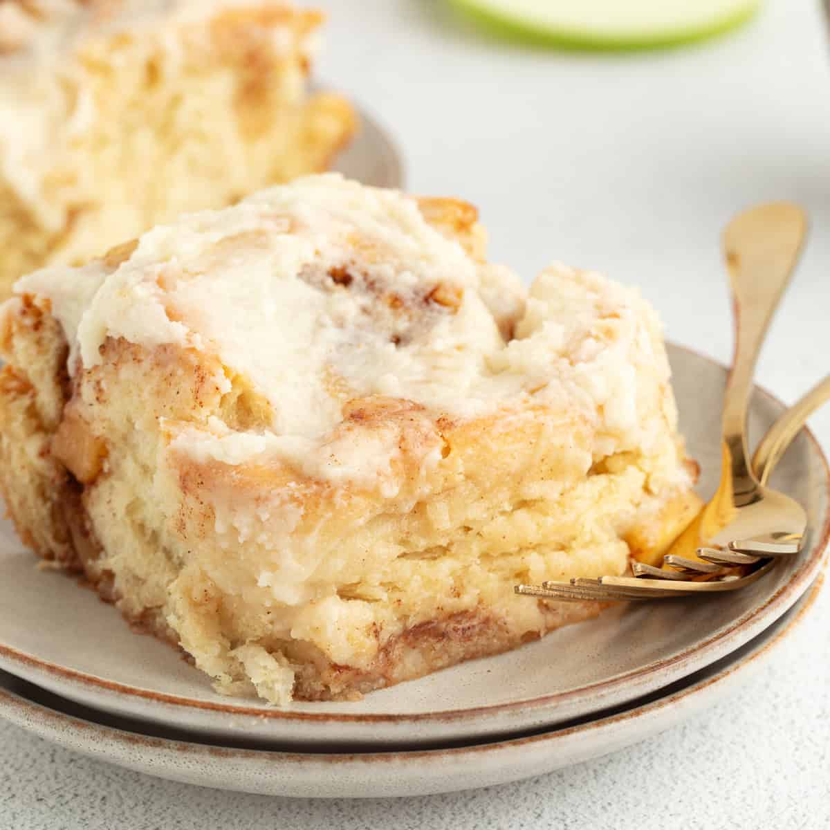 Homemade apple cinnamon rolls are golden-baked with warm cinnamon apple filling and topped with creamy brown butter cream cheese frosting. An apple cinnamon roll topped with brown butter cream cheese frosting on a plate.