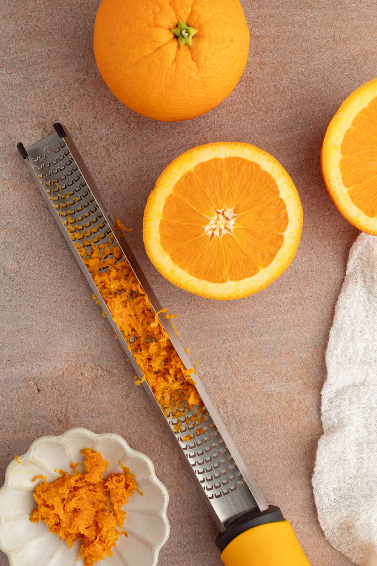 These moist cranberry orange muffins are full of real orange juice, fresh zest, and sweet-tart cranberries. So easy to make and big on flavor! Overhead view of a microplane with orange zest nest to a freshly zested orange half.