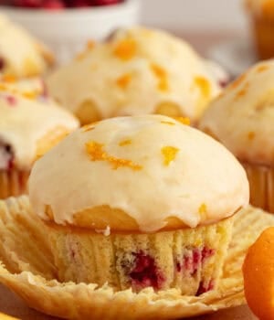 Close up of a glazed cranberry orange muffin with more muffins in the background.
