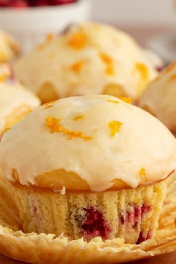 Close up of a glazed cranberry orange muffin with more muffins in the background.