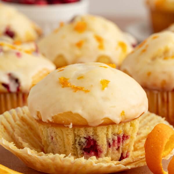 Close up of a glazed cranberry orange muffin with more muffins in the background.