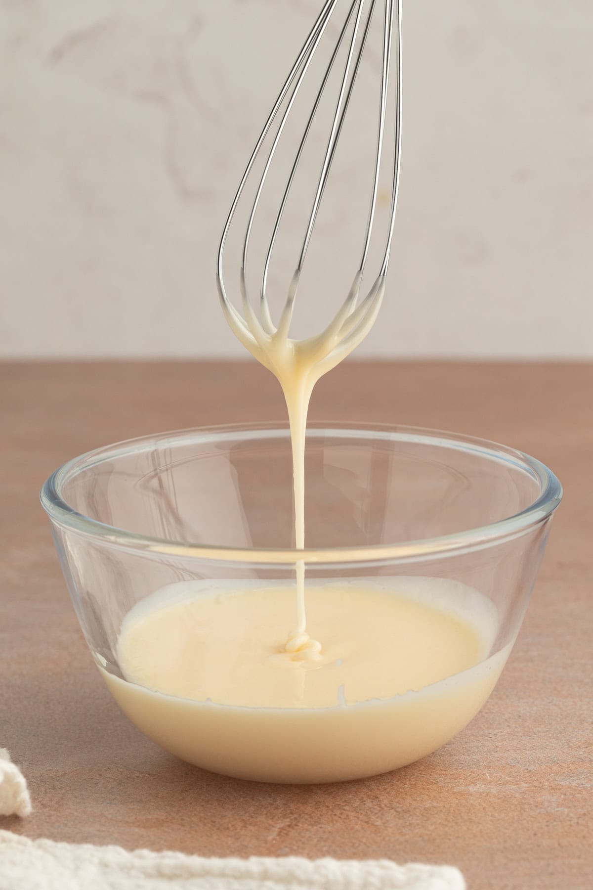 These moist cranberry orange muffins are full of real orange juice, fresh zest, and sweet-tart cranberries. So easy to make and big on flavor! A whisk drizzling orange glaze into a clear glass bowl.