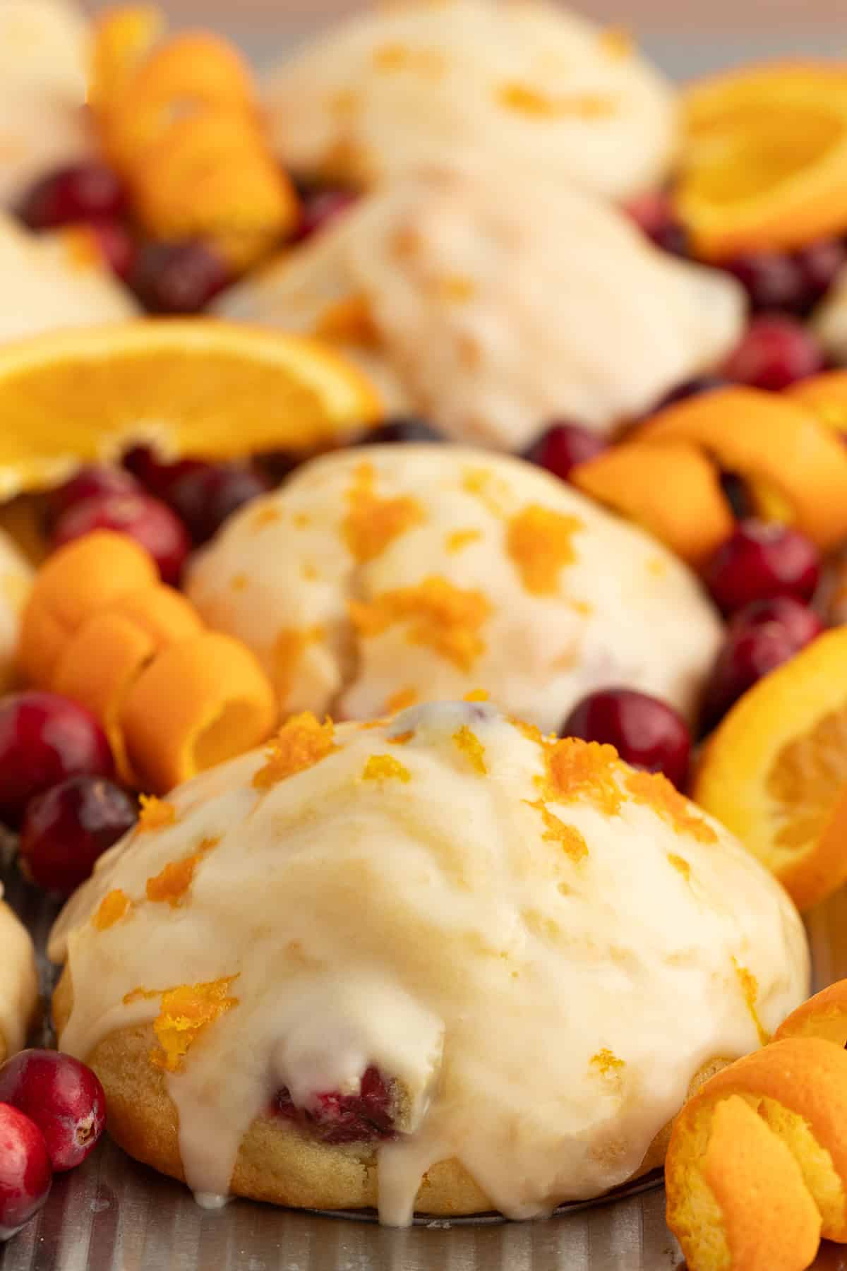 These moist cranberry orange muffins are full of real orange juice, fresh zest, and sweet-tart cranberries. So easy to make and big on flavor! Close up of baked cranberry orange muffins in a muffin tin, topped with glaze and decorated with fresh cranberries and orange rinds.