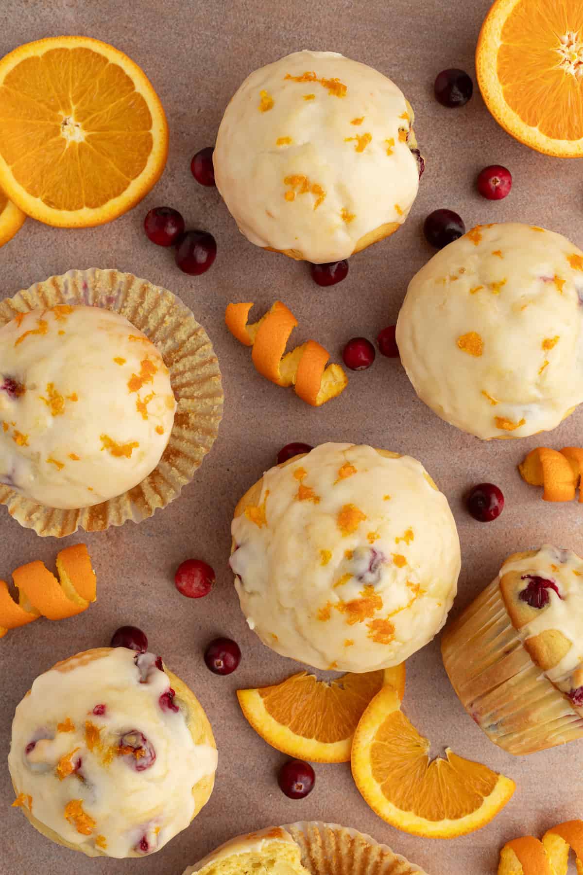 These moist cranberry orange muffins are full of real orange juice, fresh zest, and sweet-tart cranberries. So easy to make and big on flavor! Overhead view of cranberry orange muffins topped with orange glaze, surrounded by orange slices, twisted orange rinds, and scattered fresh cranberries.