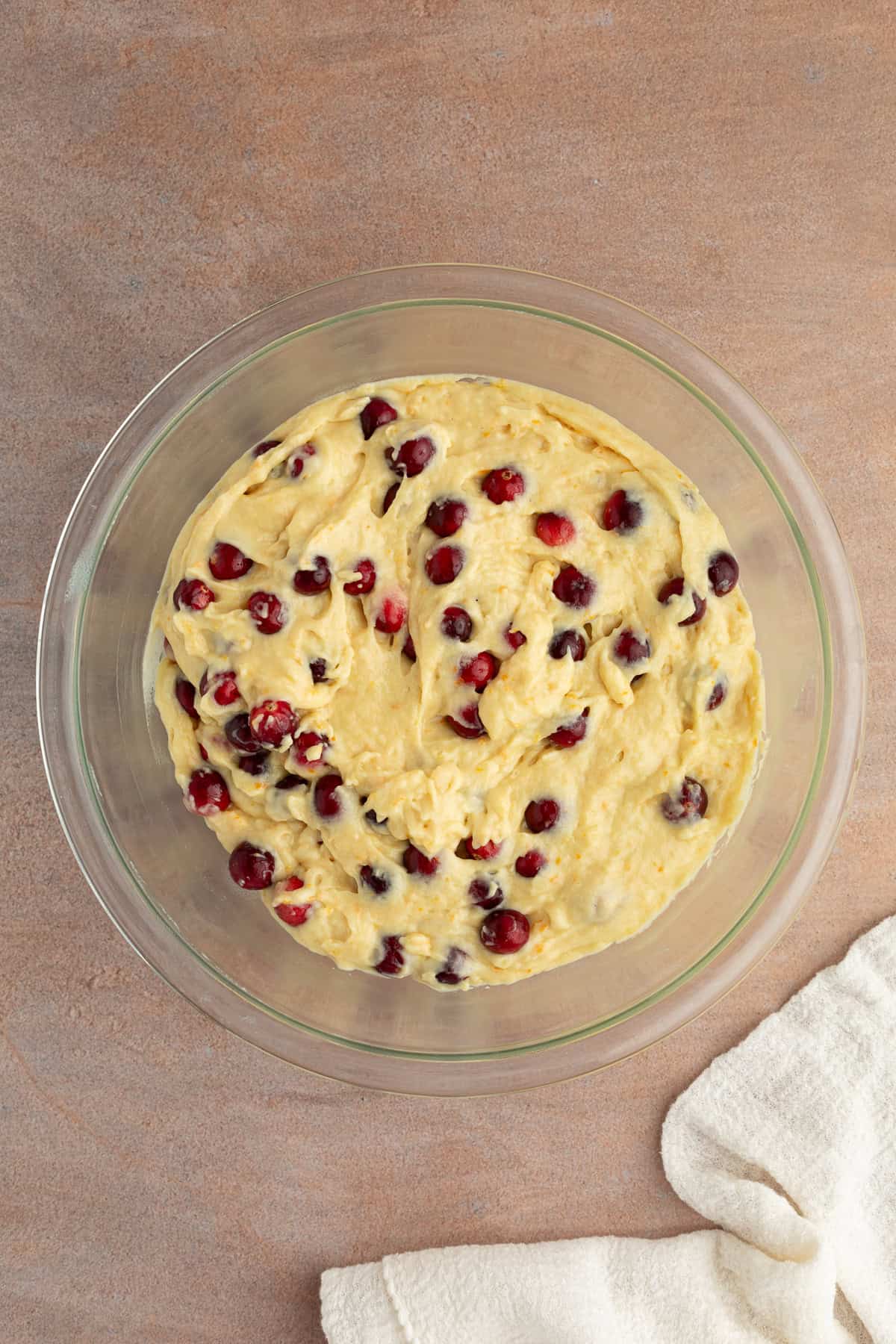 These moist cranberry orange muffins are full of real orange juice, fresh zest, and sweet-tart cranberries. So easy to make and big on flavor! Fresh cranberries folded into orange muffin batter in a glass mixing bowl.