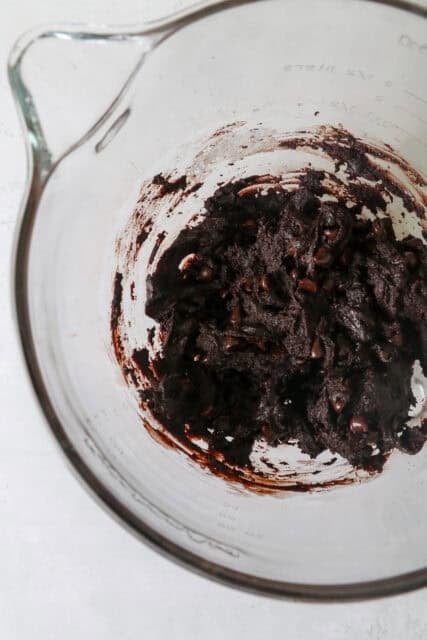 A glass mixing bowl with dark chocolate cookie dough