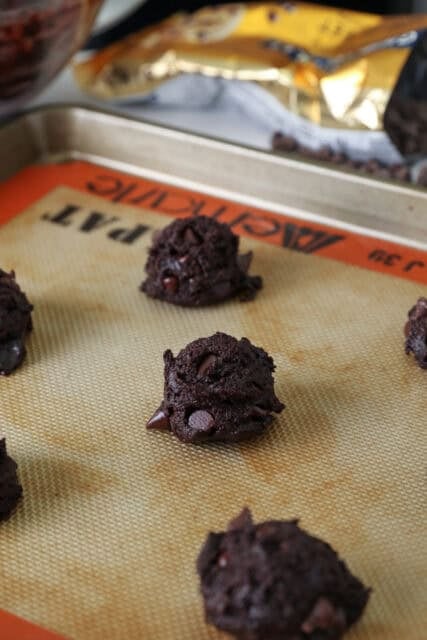 scoops of dark chocolate cookie dough on a cookie sheet with a silicone baking mat