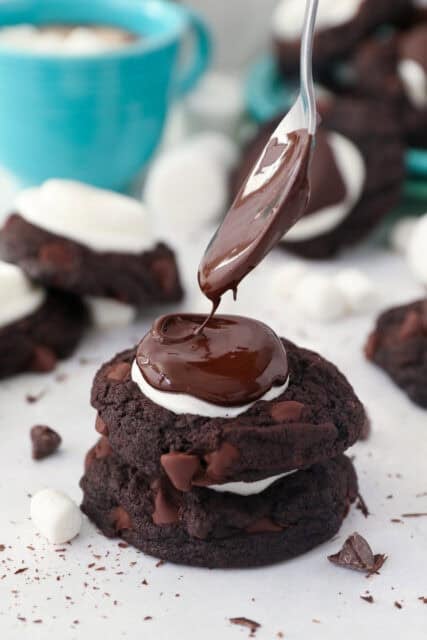 two chocolate cookies stacked with a marshmallow in the middle and chocolate glaze being dripped on top with a spoon